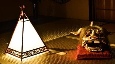 A closeup on a small, pyramid-shaped lamp and a golden mask on a red pillow in the golden room of Kaikaro Teahouse, Kanazawa